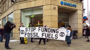 protestors stand infront of a barclays bank branch holding a banner urging divesvtment from fossil fuels